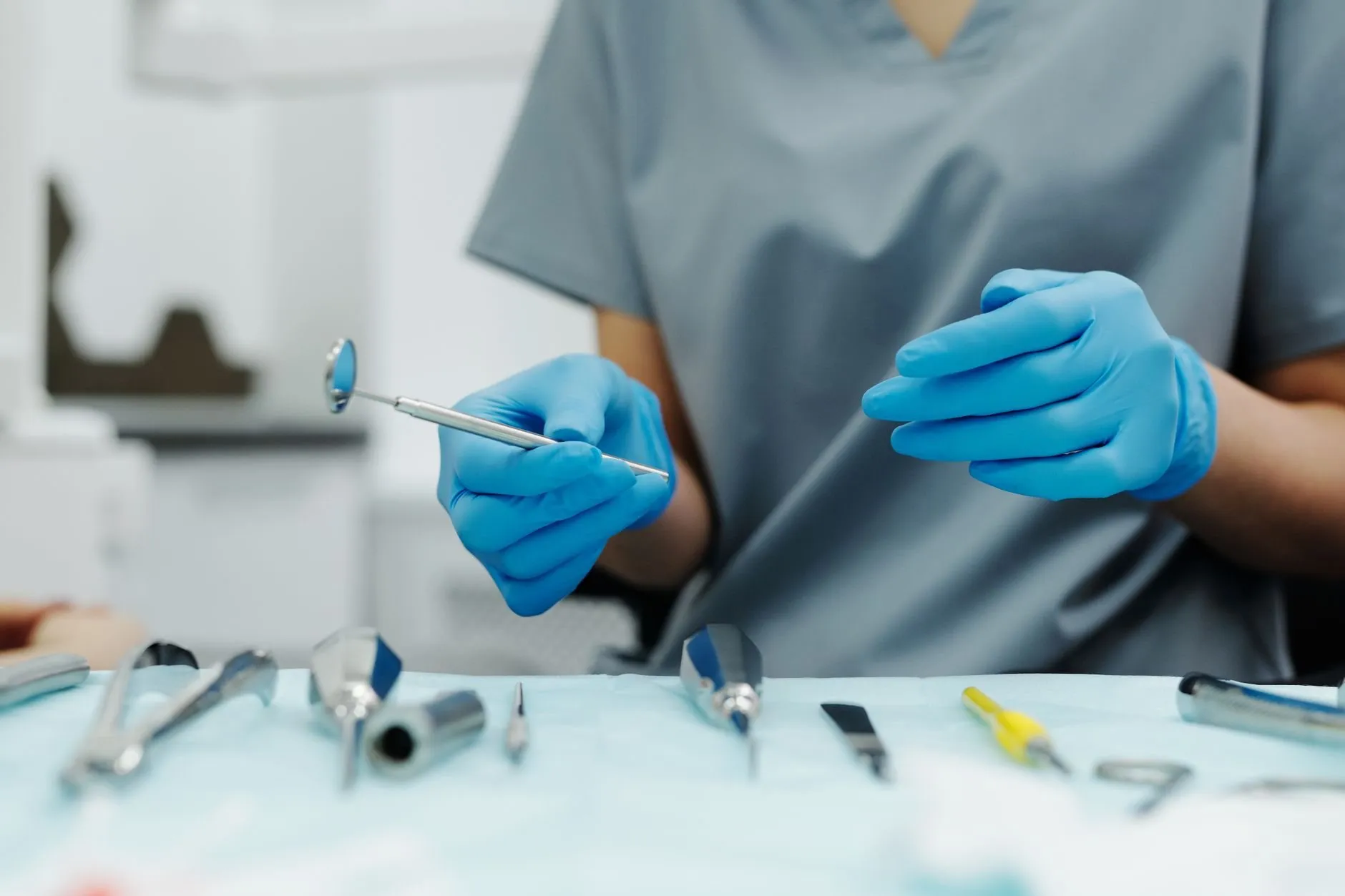 A gloved hand holding a dental mirror over a tray of instruments