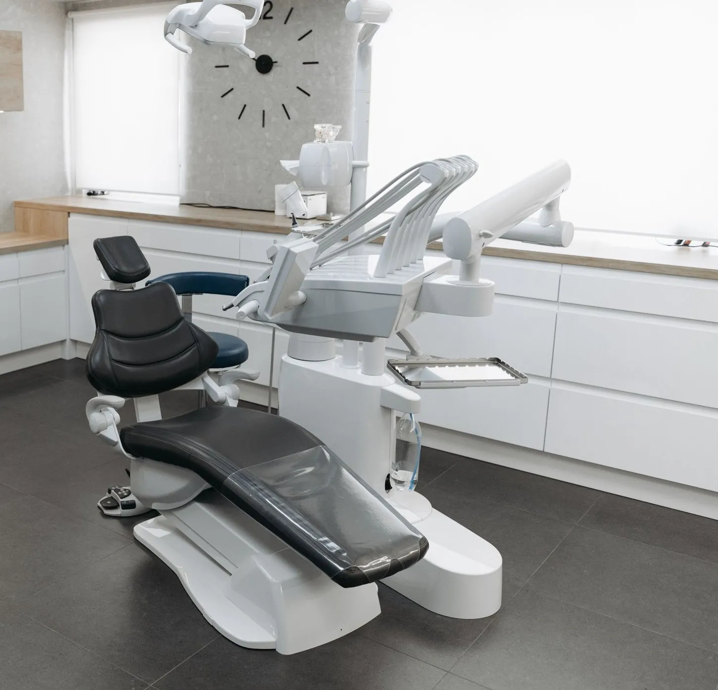 A daylit treatment room with a wood worktop, a wall clock and the dental chair reclined
