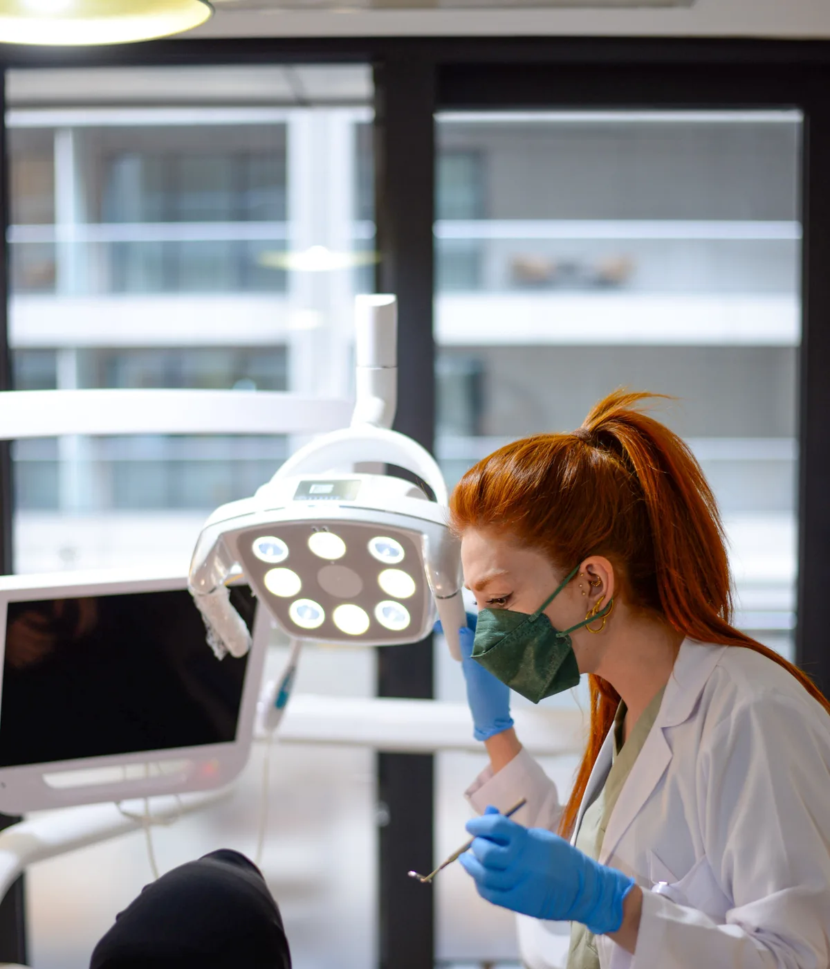 A dentist in a bright window-lit surgery, working unhurriedly at the chair.
